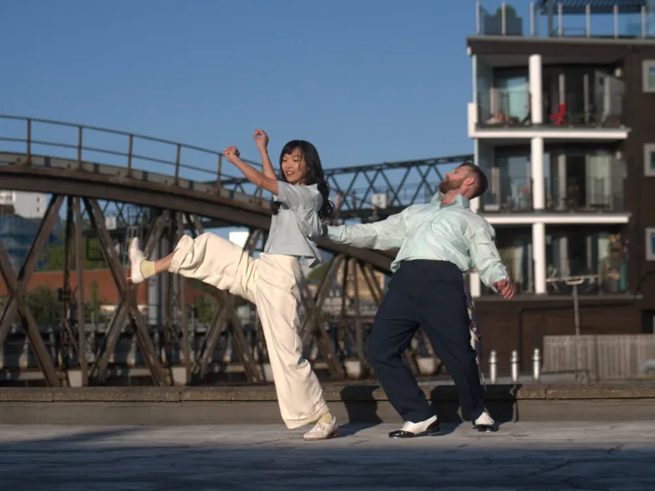 Two dancers in motion beside a city bridge in Flaws